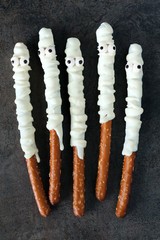 Group of Halloween mummy, candy dipped pretzel rods on black stone background