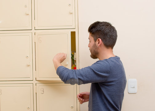 Young Handsome Man Wearing Blue Sweater Opening Metal Locker Door, Rack Of Lockers Stacked