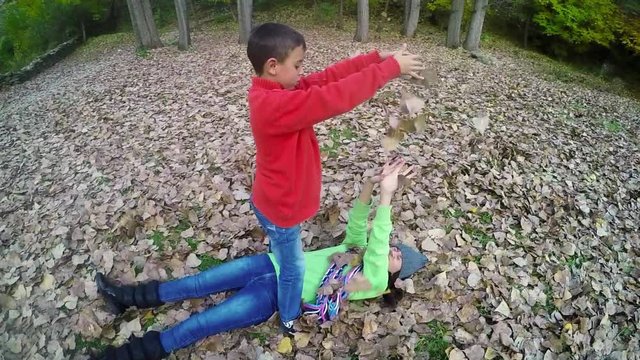 Two children play in fall park throwing leaves 