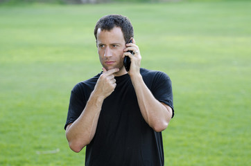 Man having a serious phone call outdoors with hand rubbing his chin.