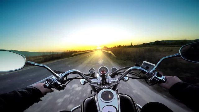 Driving motorbike on asphalt road toward heavenly sunset. POV