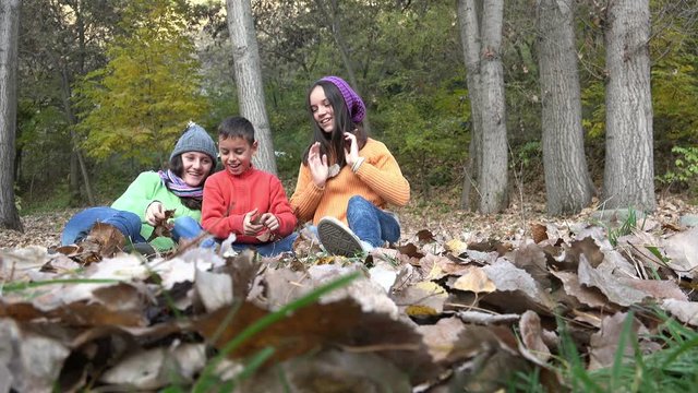 Three friends sitting, takling and playing with autumn 