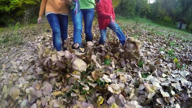 Running three children runs and kicks autumn leaves, 