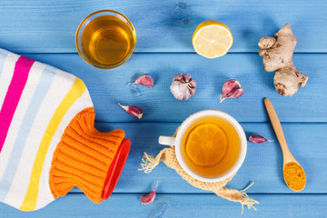 Hot water bottle, cup of tea and ingredients for preparation warming beverage
