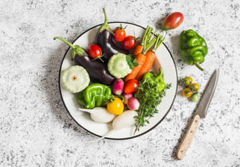 Fresh vegetables - eggplant, radish, bell pepper, tomatoes, thyme, oregano in an enamel bowl on a light background. Top view
