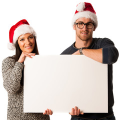 Young couple in santa hats holding blank board for advertisment.