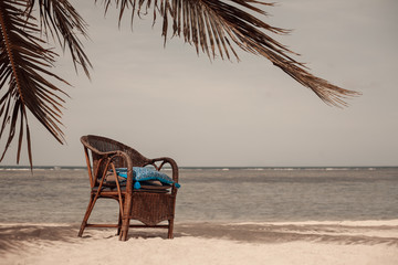 wicker chair in the shade of palm tree on beach