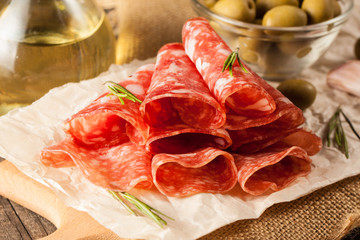 Italian salami with olives and spices on wooden background