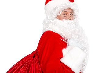 Traditional Santa Claus carrying sack with presents and looking at camera on white background
