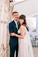 Wedding couple in love. Beautiful bride in white dress and veil and brides bouquet with handsome groom in blue suit sitting in cafe. Full lenght portrait of man and girl. Concept of wedding