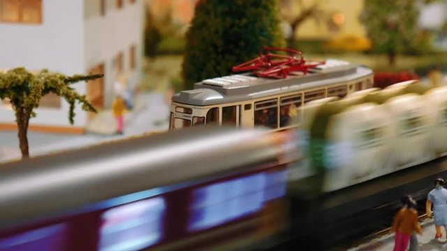 Model trains transit and a tram departs on a diorama, close up
