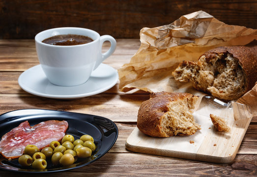 Bread, a cup of coffee , ham and olives on a wooden table lie.Focus concept.