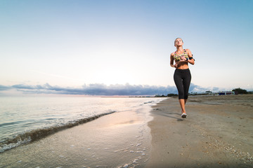 Cute fit girl jogging on beach at sunrise