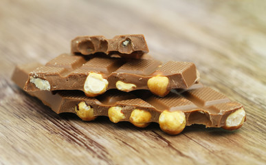 Pieces of milk chocolate with whole hazelnuts stacked up on wooden surface
