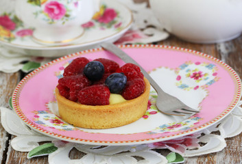Fruity tartelette with custard, fresh raspberries and blueberries on pink plate
