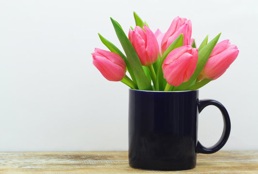 Fototapeta Pink tulips in navy blue mug on rustic surface with copy space  