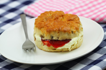 Freshly baked English scone with traditional clotted cream and strawberry jam on white plate
