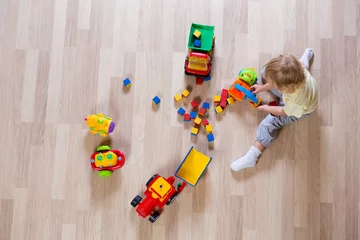 Fotobehang Lego Little blond kid boy playing with colorful car toys on floor top view  © Andrey Kuzmin