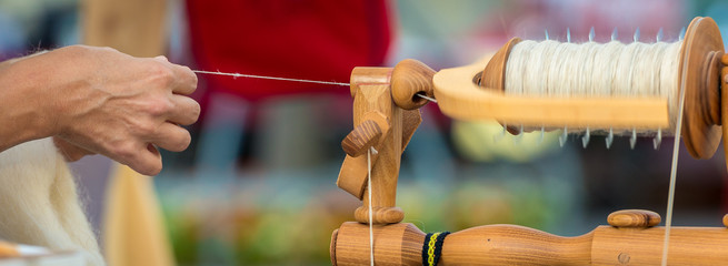 Frau spinnt an einem Spinnrad Fasern zu einem Faden