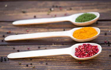 Three wooden spoons with colorful spices on wooden background