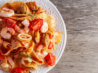 Tasty Pappardelle pasta with shrimp, Squid, mussel, tomatoes on wooden table
