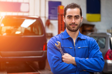 Young attractive mechanic working at the garage - obrazy, fototapety, plakaty