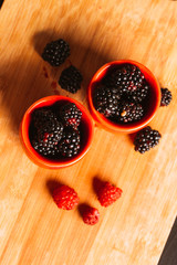 Fototapeta na wymiar Blackberries in a cup on blurred background of wooden planks