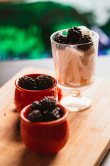 Blackberry ice cream in a cup and  glass on  background of wooden boards   blurred green