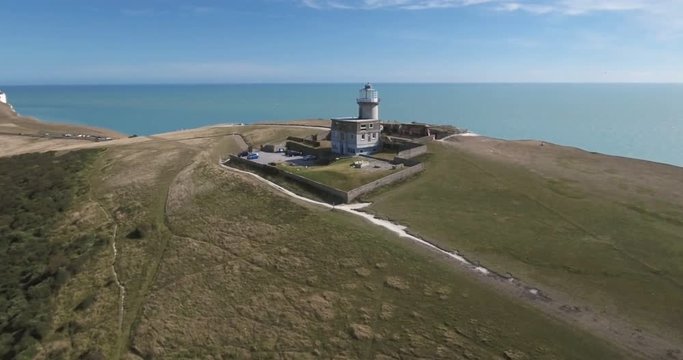 Aerial pull out view of a lighthouse on a cliff area by the sea