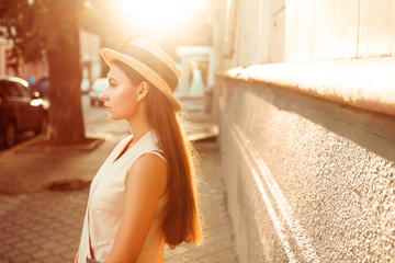 Fashionable and beautiful girl in a hat walks through sunny city