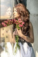 Haired girl in a wedding dress and makeup with a festive with a bouquet of roses
