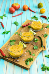 Cold fresh homemade tomato soup gazpacho in glasses on cutting board and ingredients with red, yellow tomatoes, celery, lime and chili peppers over rustic turquoise wooden background, close-up