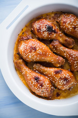 Baked spicy chicken legs with sesame on blue wooden background top view.