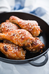 Baked spicy chicken legs with sesame in cast iron frying pan on white background close up.