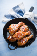 Baked spicy chicken legs with sesame in cast iron frying pan on blue wooden background close up.