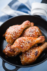 Baked spicy chicken legs with sesame in cast iron frying pan on blue wooden background close up.