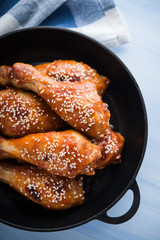 Baked spicy chicken legs with sesame in cast iron frying pan on blue wooden background top view.