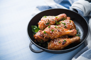 Baked spicy chicken legs with sesame and parsley in cast iron frying pan on blue wooden background close up.