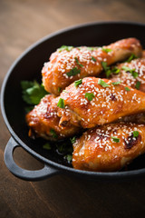 Baked spicy chicken legs with sesame and parsley in cast iron frying pan on dark wooden background close up.