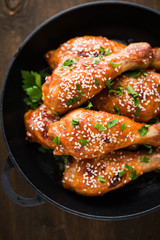 Baked spicy chicken legs with sesame and parsley in cast iron frying pan on dark wooden background top view.