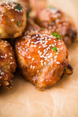 Baked spicy chicken legs with sesame and parsley on paper background close up.