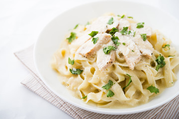 Pasta fettuccine alfredo with chicken, parmesan and parsley on white background close up. Italian cuisine.