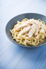 Pasta fettuccine alfredo with chicken and parmesan on blue wooden background close up. Italian cuisine.