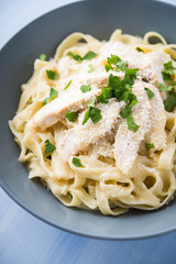 Pasta fettuccine alfredo with chicken, parmesan and parsley on blue wood background close up. Italian cuisine.