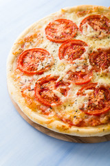 Pizza with tomato, cheese and dry basil on blue wooden background close up. Italian cuisine.