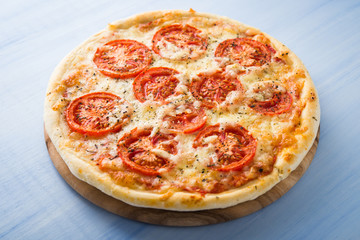 Pizza with tomato, cheese and dry basil on blue wooden background close up. Italian cuisine.