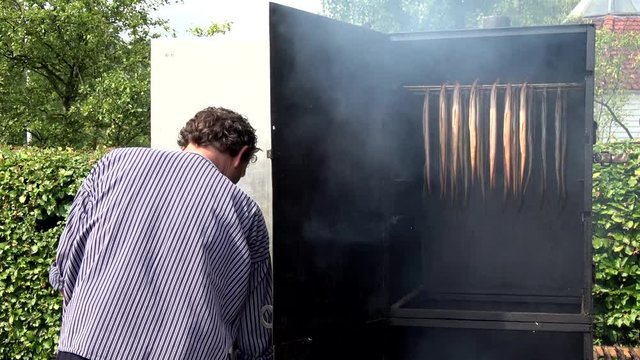Smoking eel man checking on elongated fish in smoking cabinet in some countries smoked eel is considered a delicacy for example in The Netherlands Holland the Dutch people love gerookte paling 4k