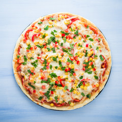 Pizza with mozzarella cheese, chicken, sweet corn, sweet pepper and parsley on blue wooden background top view. Italian cuisine.