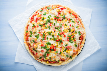 Pizza with mozzarella cheese, chicken, sweet corn, sweet pepper and parsley on blue wooden background top view. Italian cuisine.