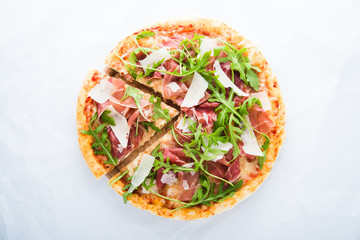 Sliced pizza with prosciutto (parma ham), arugula (salad rocket) and parmesan on white background...